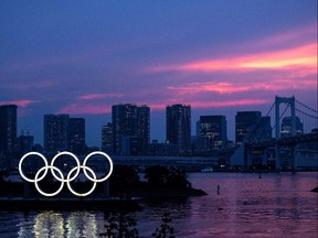 A general view shows the Olympic rings lit up at dusk, with the Rainbow bridge in the background, on the Odaiba waterfront in Tokyo on July 12, 2021. (Photo by Charly TRIBALLEAU / AFP)