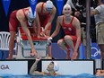Canada's Taylor Ruck, Canada's Sydney Pickrem and Canada's Margaret Macneil cheer on teammate Canada's Kayla Sanchez to win a heat for the women's 4x100m medley relay swimming event during the Tokyo 2020 Olympic Games at the Tokyo Aquatics Centre in Tokyo on July 30, 2021. (Photo by Oli SCARFF / AFP)