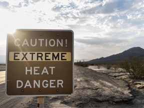 With the Amargosa Mountain Range in the background at sunrise, a sign warns park visitors of "extreme heat danger" along Highway 190 on Sunday. MUST CREDIT: Washington Post photo by Melina Mara.