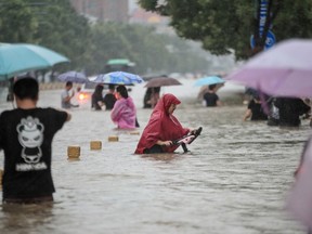 This photo taken on July 20, 2021 shows people wading through flood waters along a street following heavy rains in Zhengzhou in China's central Henan province.