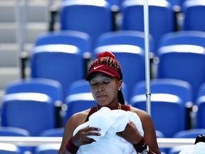 Naomi Osaka, sitting under an umbrella, wipes off sweat during a break in her match at Ariake Tennis Park on Sunday. MUST CREDIT: Japan News-Yomiuri