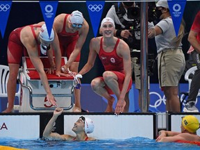 Canada's Taylor Ruck, Canada's Sydney Pickrem aand Canada's Margaret Macneil cheer on teammate Canada's Kayla Sanchez to win a heat for the women's 4x100m medley relay swimming event during the Tokyo 2020 Olympic Games at the Tokyo Aquatics Centre in Tokyo on July 30, 2021.