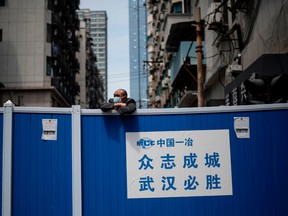 A man wearing a face mask looks over a barricade set up to keep people out of a residential compound in Wuhan in China's central Hubei province on April 14, 2020.