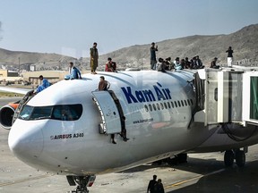 Afghan people climb atop a plane as they wait at the airport in Kabul on August 16, 2021, after a stunningly swift end to Afghanistan's 20-year war, as thousands of people mobbed the city's airport trying to flee the group's feared hardline brand of Islamist rule.