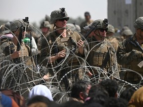 U.S. soldiers stand guard behind barbed wire as Afghans sit on a roadside near the military part of the airport in Kabul on Aug. 20.
