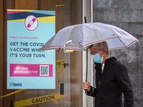Ein Fußgänger mit Maske geht am Donnerstag, den 8. Juli 2021 an der Ecke Church Street und Queen Street an einem Plakat vorbei, das die Einwohner von Toronto ermutigt, sich den COVID-19-Impfstoff zu holen, wenn sie an der Reihe sind.