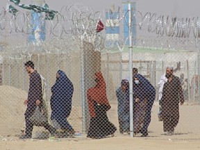 Afghan nationals walk along a fenced corridor as they enter Pakistan through the Pakistan-Afghanistan border crossing point in Chaman.