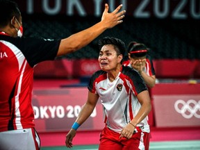 Indonesia's Apriyani Rahayu (R) celebrates with a coach after winning with Indonesia's Greysia Polii in their women's doubles badminton final match against China's Jia Yifan and China's Chen Qingchen during the Tokyo 2020 Olympic Games at the Musashino Forest Sports Plaza in Tokyo on August 2, 2021.