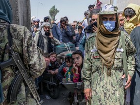 Taliban members stand next to people rushing to pass to Pakistan from the Afghanistan border in Spin Boldak on Sept. 25, 2021.