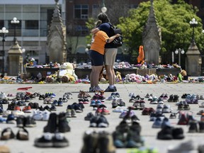 People embrace in front of the Centennial Flame on Parliament Hill at a memorial earlier this summer for the 215 children whose remains were found at the grounds of the former Kamloops Indian Residential School at Tk’emlups te Secwépemc First Nation in Kamloops, B.C.