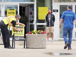 An Elections Canada poll worker attaches a sign to a chair outside a polling station at Assiniboia Downs in Winnipeg on Mon., Sept. 20, 2021.