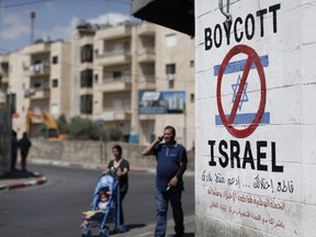 Palestinians walk past a sign painted on a wall in the West Bank town of Bethlehem calling for a boycott of Israeli products coming from Jewish settlements.