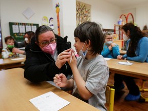 A parent helps a child perform an antigen rapid test at an elementary school