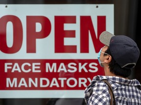 A pedestrian wearing a mask reads signage stating “Open Face Masks Mandatory” in Toronto during the pandemic. (Peter J. Thompson/National Post