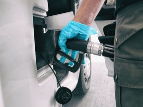 A man at a gas station wearing a blue medical glove to grab the refueling nozzle handle.