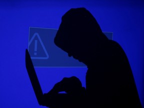 FILE PHOTO: Hooded man holds laptop computer as blue screen with an exclamation mark is projected on him in this illustration picture