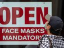 Ein Fußgänger, der eine Maske trägt, liest während der Pandemie in Toronto ein Schild mit der Aufschrift „Offene Gesichtsmasken obligatorisch“.