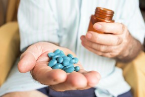 closeup of an old caucasian man with a pile of blue pills in his hand