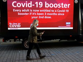 A woman wearing a face mask walks past a mobile advertising screen encouraging people to get a COVID-19 booster vaccine in Bolton, Britain, December 18, 2021. REUTERS/Phil Noble