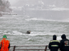 People look at a car submerged in rapids near the edge of American Falls in Niagara Falls, New York, December 8, 2021.