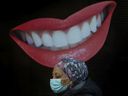 A pedestrian wearing a mask walks past an animated smiling mouth and teeth out front of Dorval Dental on Toronto's Bloor Street West during the COVID 19 pandemic in Toronto, on Dec. 14, 2021. 