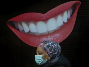 A pedestrian wearing a mask walks past an animated smiling mouth and teeth out front of Dorval Dental on Toronto's Bloor Street West during the COVID 19 pandemic in Toronto, on Dec. 14, 2021.