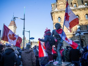 A protester stands on the Terry Fox statue to which an upside down flag of Canada was added.