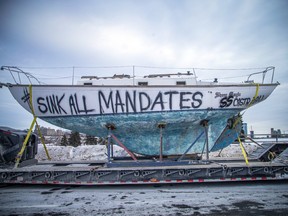 Trucks parked on the Sir John A. MacDonald Parkway into Ottawa on Sunday, January 30, 2022, include a trailer-mounted sail boat with “sink all mandates” painted on it.