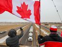 Unterstützer des „Freiheitskonvois“ von Truckern versammelten sich am Montag, den 24. Januar 2022, auf einer Überführung über den Trans-Canada Highway östlich von Calgary. Die Trucker fahren quer durch Kanada nach Ottawa, um gegen das COVID-19-Impfmandat der Bundesregierung für Cross zu protestieren -Grenzlastfahrer