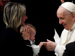 Pope Francis reaches out to a baby's hand as he meets with attendees during the weekly general general audience at Paul-VI Hall in the Vatican on January 26, 2021