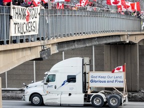 Unterstützer stehen auf einer Fußgängerbrücke in Mississauga, Ontario, mit Blick auf die QEW, während während der COVID-19-Pandemie am Donnerstag, dem 27. Januar 2022 Konvoi-Protestlastwagen darunter vorbeifahren.