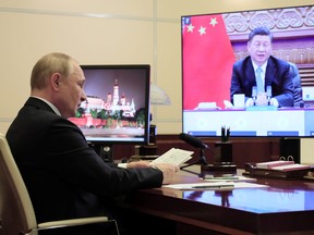 Russian President Vladimir Putin sits in front of a screen displaying Chinese President Xi Jinping as he attends the G20 summit via a video link at his residence outside Moscow, Russia October 31, 2021.