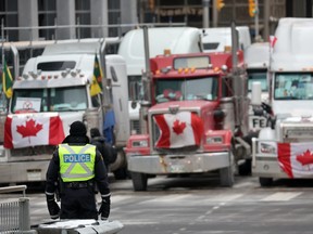 Ein Polizist steht Wache in der Nähe von Lastwagen, die an einer Blockade der Straßen der Innenstadt in der Nähe des Parlamentsgebäudes teilnehmen, während eine Demonstration, die von Lastwagenfahrern angeführt wird, die gegen Impfmandate protestieren, am 16. Februar 2022 in Ottawa fortgesetzt wird.