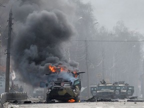 This photograph taken on February 27, 2022 shows a Russian Armoured personnel carrier (APC) burning next to unidentified soldier's body during fight with the Ukrainian armed forces in Kharkiv. - Ukrainian forces secured full control of Kharkiv on February 27, 2022 following street fighting with Russian troops in the country's second biggest city, the local governor said.