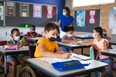 Disabled caucasian boy wearing face mask studying while sitting on wheelchair at elementary school. education back to school health safety during covid19 coronavirus pandemic.