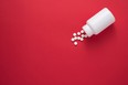 Pills spilling from a bottle. Red background. View from the top