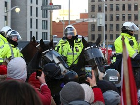 Demonstranten stehen vor kanadischen Polizisten auf Pferden, während Trucker und Unterstützer am 18. Februar 2022 in Ottawa gegen Impfmandate protestieren.