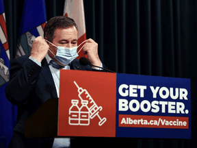 Alberta Premier Jason Kenney takes off his mask before providing a COVID-19 update. Kenney says his government is 'very eager to drop' public-health restrictions.