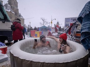 Protesters Gabriel (L) and Jean-Philippe (R) sit in a hot tub between trucks during a protest against pandemic health rules and the Trudeau government, outside Parliament in Ottawa, Ontario, on February 12, 2022. (Photo by Ed JONES /AFP)