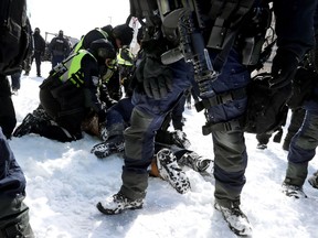 Ein schwer bewaffneter Beamter hält Wache, während drei Polizisten am Freitag einen Demonstranten in der Innenstadt von Ottawa festhalten.