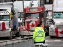 Ein Polizist steht Wache in der Nähe von Lastwagen, die am 16. Februar 2022 an einer Blockade der Straßen der Innenstadt in der Nähe der Parlamentsgebäude in Ottawa teilnehmen.