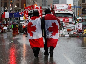 People walk with Canadian flags near signage of support for the Freedom Convoy, as truckers and supporters continue to protest in Ottawa on Feb. 17, 2022.
