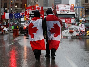 People walk with Canadian flags near signage of support for the Freedom Convoy, as truckers and supporters protest vaccine mandates and other COVID measures in Ottawa on Feb. 17, 2022.