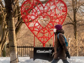 A pedestrian wearing a mask walks past a heart with writing stating “Show Love TO” on Toronto’s Danforth Avenue during the COVID-19 pandemic, February 8, 2022.