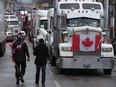 Protesters walk between trucks parked along Wellington Street in downtown Ottawa as the "Freedom Convoy" occupation protesting vaccine mandates and other COVID measures continues on Feb. 10, 2022.