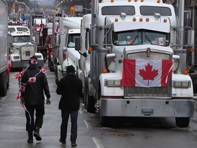 Demonstranten gehen zwischen Lastwagen entlang, die entlang der Wellington Street in der Innenstadt von Ottawa geparkt sind 