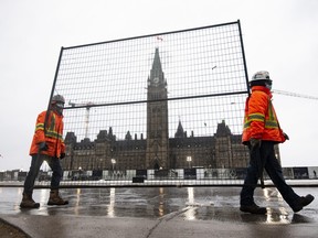 Crews carry a piece of fencing to shore up the existing gates along Wellington Street on Parliament Hill, on Thursday.