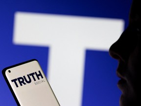The Truth social network logo is seen displayed behind a woman holding a smartphone in this picture illustration taken February 21, 2022. REUTERS/Dado Ruvic/Illustration