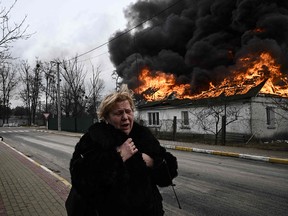 A distraught woman stands in front of a house burning after being shelled in the city of Irpin, outside Kyiv, on March 4, 2022, as Russia's invasion of Ukraine continues.