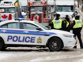 Police patrol a barricade while vehicles block downtown streets as truckers and supporters continue to protest vaccine mandates and other COVID measures in Ottawa on Feb. 3, 2022.